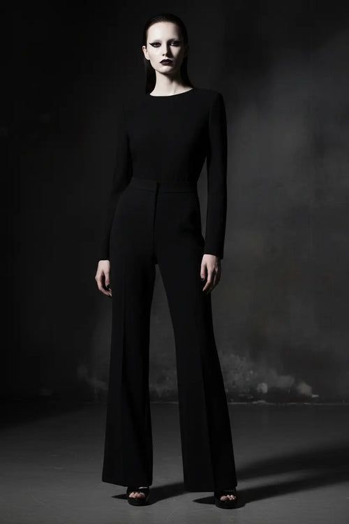 Person wearing a black shirt and wide leg pants against a dark background