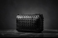 Black studded handbag on a dark surface with a dark background
