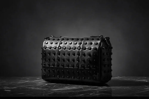 Black studded handbag on a dark surface with a dark background